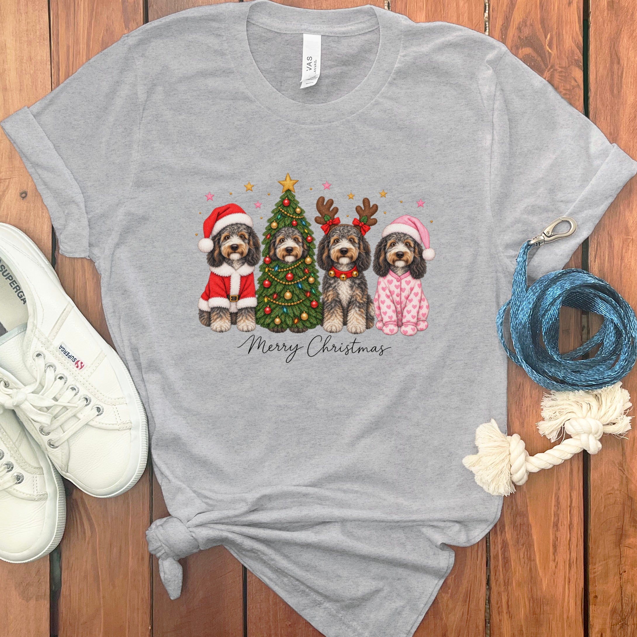A heather gray t-shirt featuring a Christmas graphic of four dogs, a decorated tree, and Merry Christmas text.