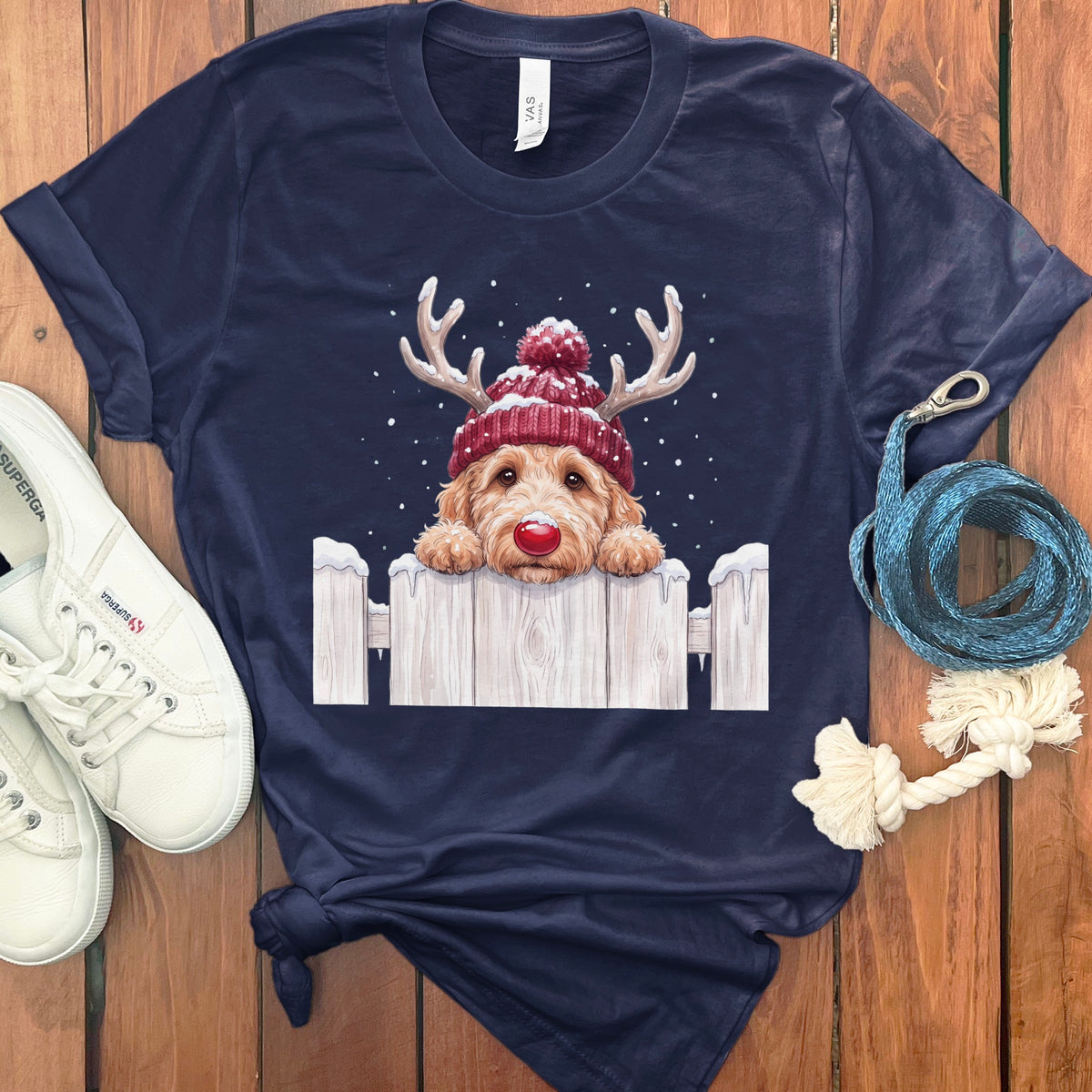 Dog wearing a red reindeer hat and red nose peeking over a snowy fence.