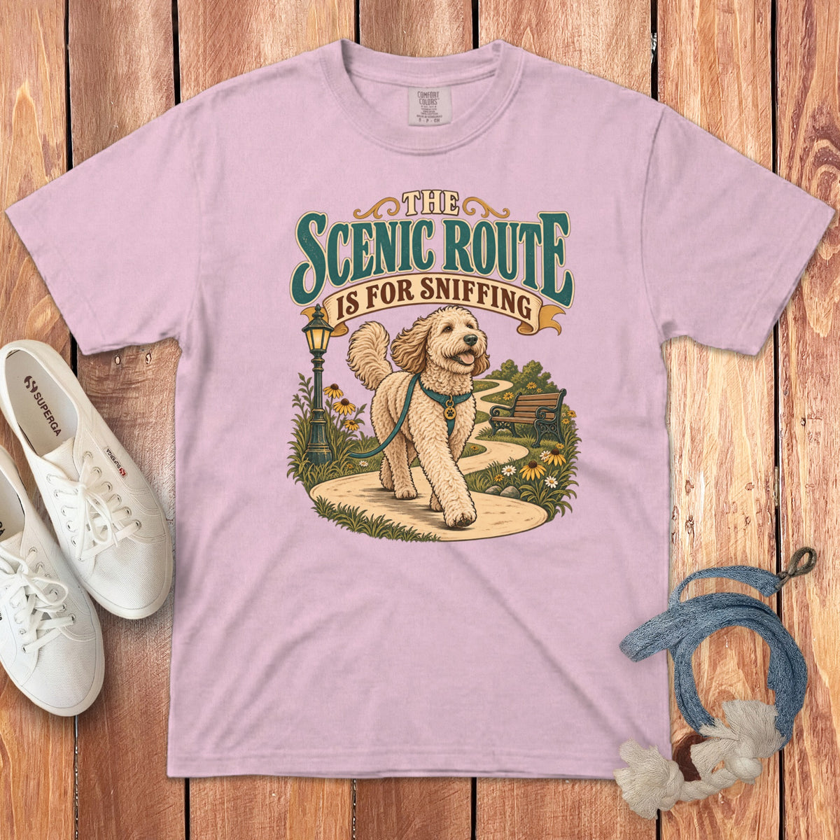 Light pink t-shirt featuring a graphic of a golden doodle walking along a park path, with the text The Scenic Route Is For Sniffing.
