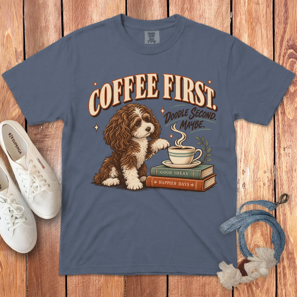 Slate blue t-shirt featuring a graphic of a brown and white dog next to a coffee cup on books, with the text COFFEE FIRST. DOODLE SECOND. MAYBE.
