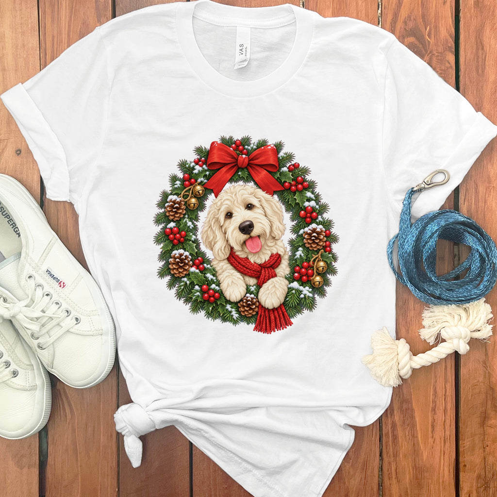 A white t-shirt featuring a doodle dog graphic inside a Christmas wreath on a wooden surface.