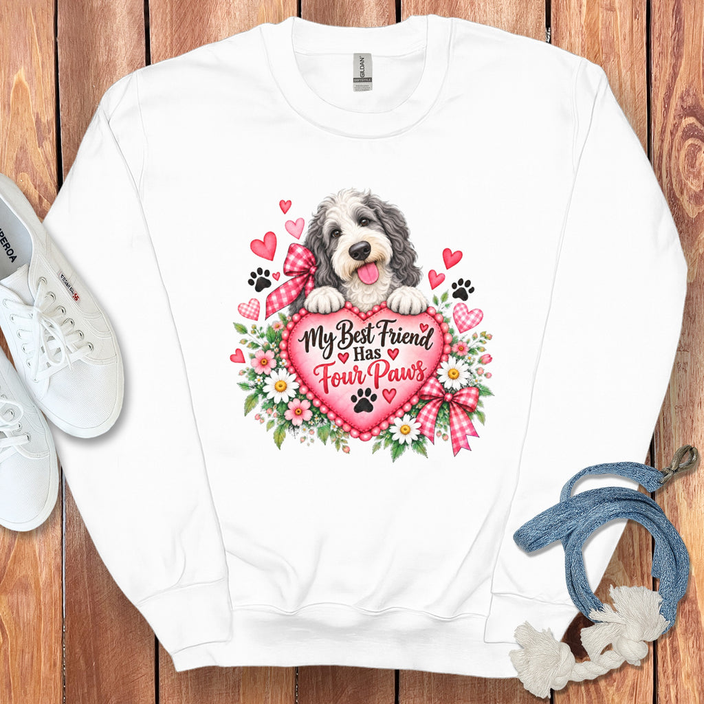 A white crewneck sweatshirt features a graphic of a shaggy dog behind a pink heart with flowers, paw prints, and the text My Best Friend Has Four Paws.
