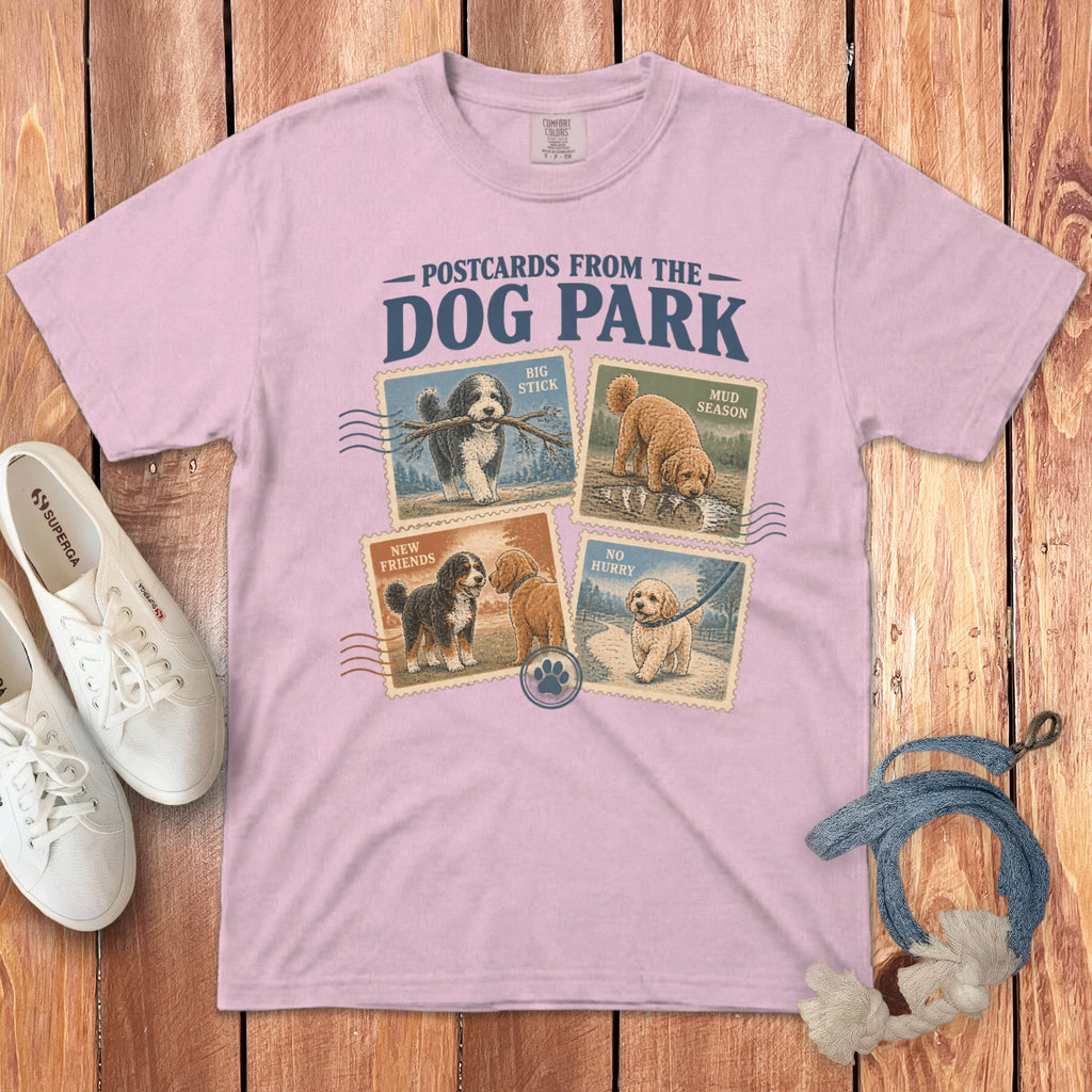A light pink t-shirt with a graphic of four dog stamp designs and the text "Postcards From The Dog Park".