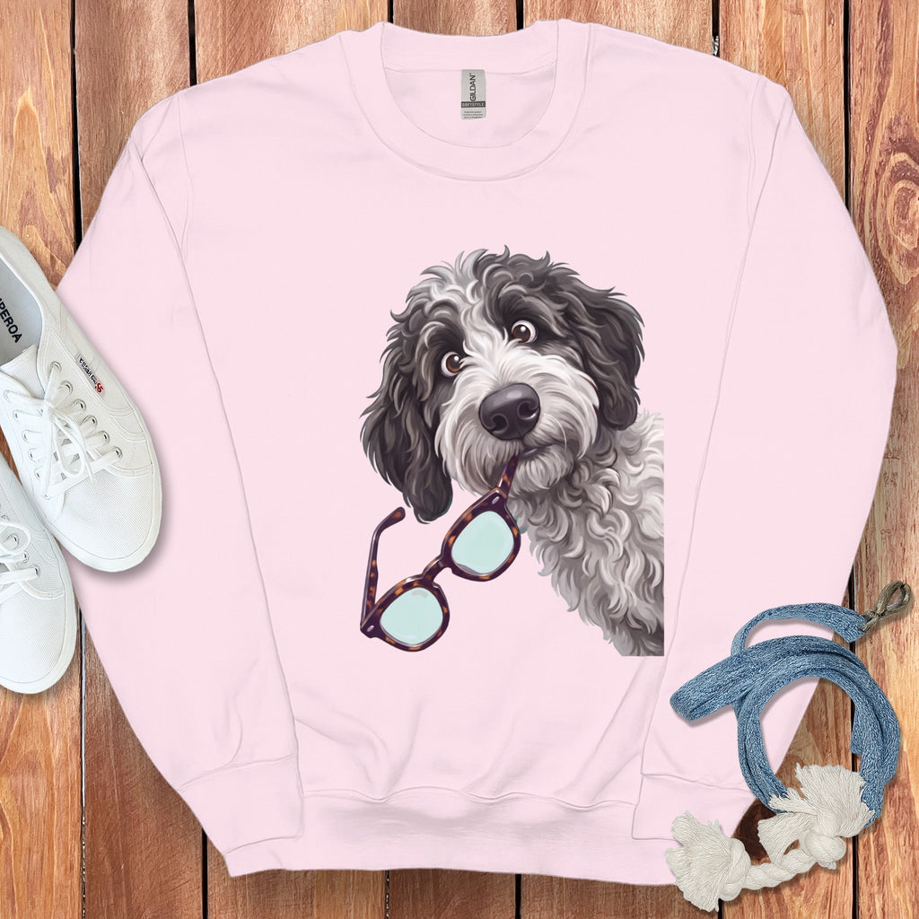 A light pink crewneck sweatshirt features an illustrated black and white doodle dog biting tortoise-shell glasses.