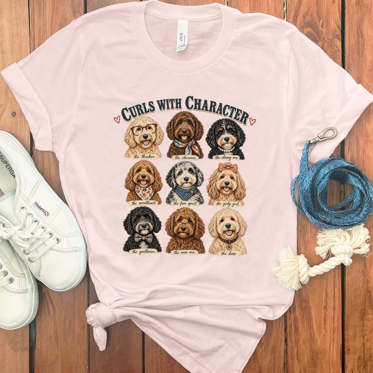 Pink t-shirt with nine doodle dog portraits and "Curls With Character" text.