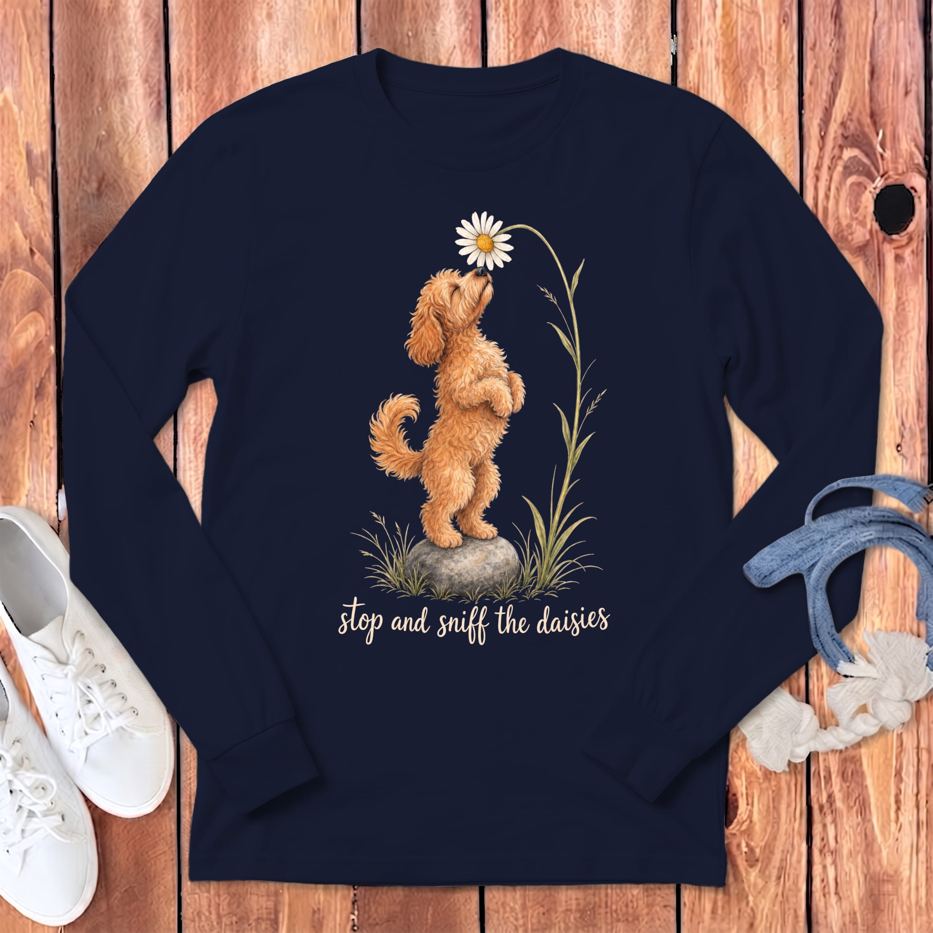 A doodle dog sniffs a daisy on a navy long-sleeve shirt with text.