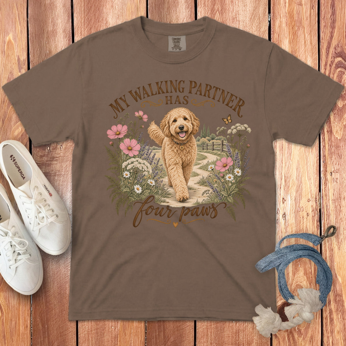 Brown t-shirt featuring a golden doodle graphic, text reading My walking partner has four paws, surrounded by flowers.